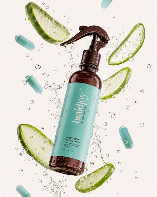 Amber braidjoy Daily Dew hydrating hair mist with a teal label surrounded by splashing water, aloe slices, and vitamin capsules, highlighting lightweight hydration, silk protein, and vitamins for healthier hair while braided.