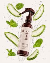 Amber braidjoy Daily Dew hydrating hair mist with a teal label surrounded by splashing water, aloe slices, and vitamin capsules, highlighting lightweight hydration, silk protein, and vitamins for healthier hair while braided.