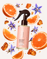 Braidjoy Halo Mist braid fragrance and finishing spray in Main Squeeze, surrounded by orange slices, purple flowers, and amber droplets, designed to refresh braids, neutralize odor, and add a lightweight salon-fresh shine.