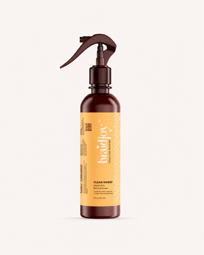 Amber braidjoy Clean Sweep spray bottle with a yellow label on a light background, designed as a pre-shampoo scalp detox that breaks down product buildup, dandruff, and dirt knots while leaving the scalp refreshed with a lemony-mint feel.