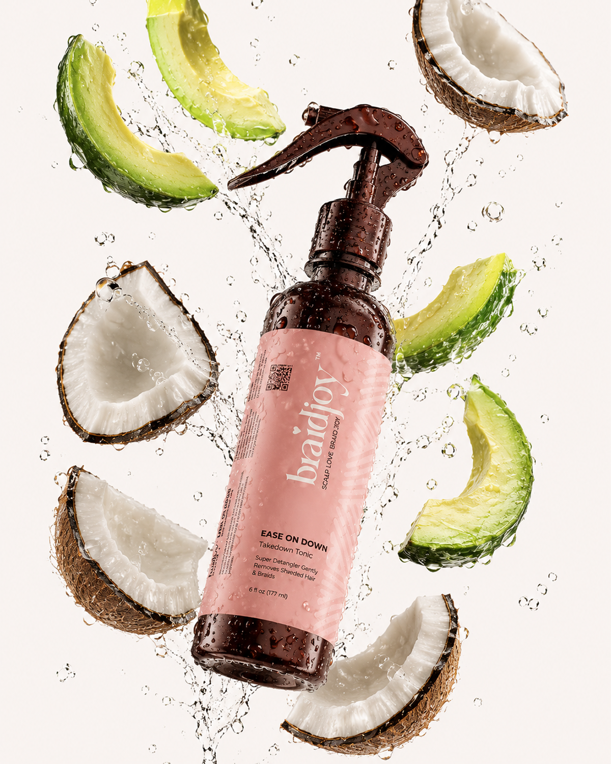 Amber braidjoy Ease on Down spray bottle with a pink label surrounded by splashing water, coconut pieces, and avocado slices, highlighting a gentle takedown tonic for softening shed hair and removing braids with less breakage.
